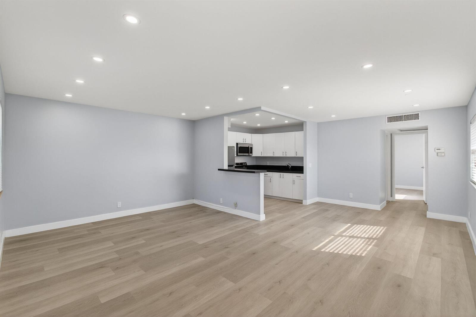 An open-concept living area with light wood floors, gray walls, and a pass-through kitchen — 171 Monaco D, Delray Beach FL 33446, DELRAY BEACH, FL