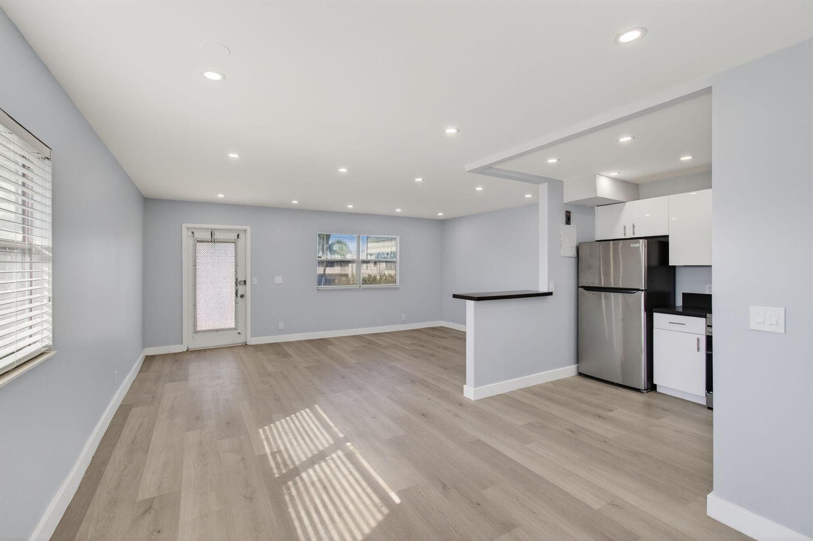 A bright, open-concept living area with light blue walls, wood-look flooring, and a small kitchen — 171 Monaco D, Delray Beach FL 33446, DELRAY BEACH, FL