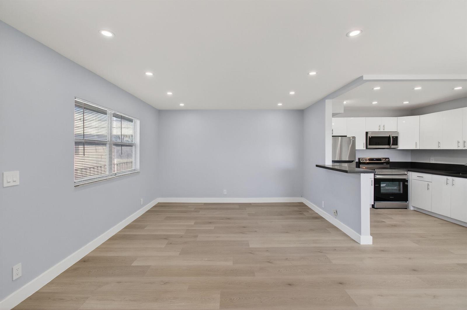 An open-concept living area features light gray walls, wood-look flooring, and an adjacent white kitchen — 171 Monaco D, Delray Beach FL 33446, DELRAY BEACH, FL