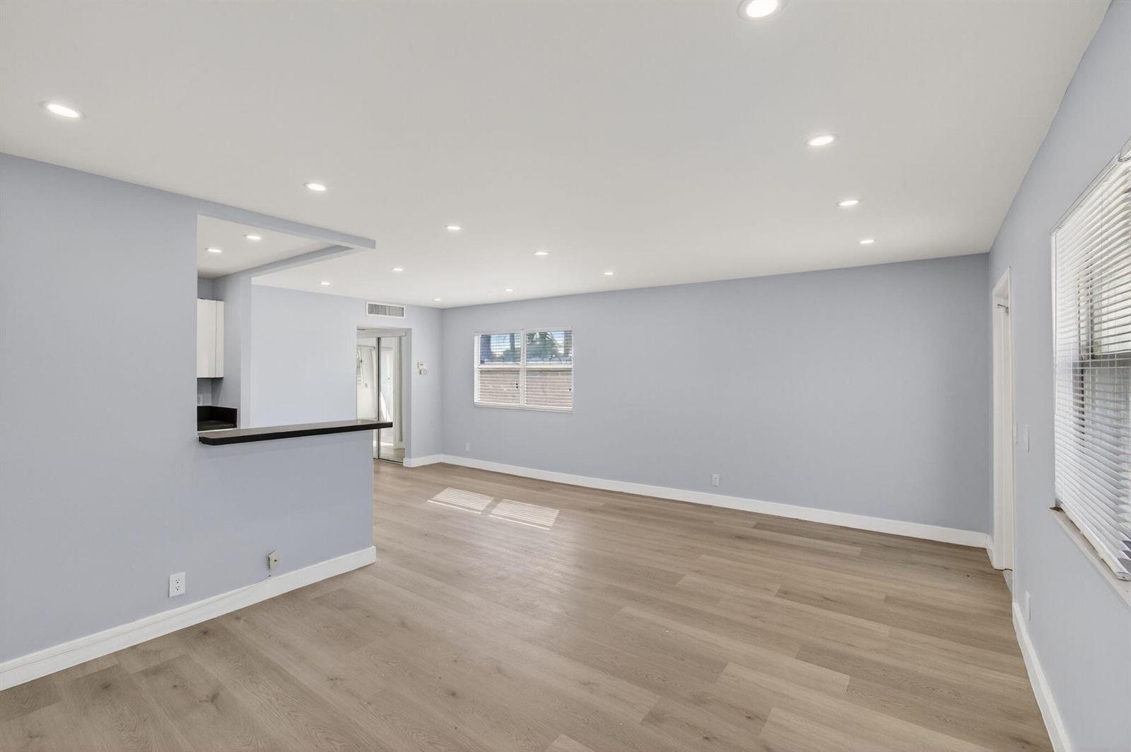 An empty living room with light blue walls, wood-look flooring, and a kitchen pass-through window — 171 Monaco D, Delray Beach FL 33446, DELRAY BEACH, FL