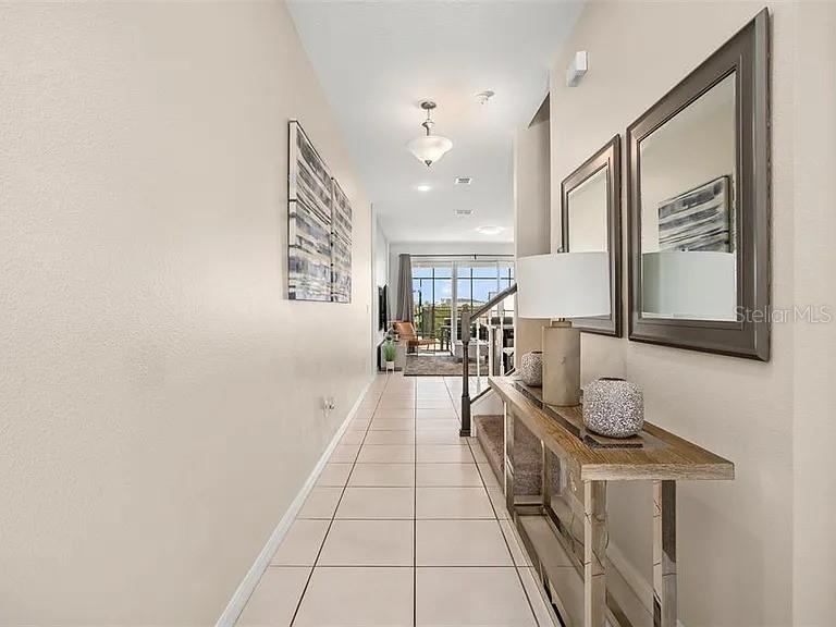 A tiled hallway features a console table with a lamp and mirrors against the wall — 1521 CAREY PALM CIRCLE, KISSIMMEE, FL