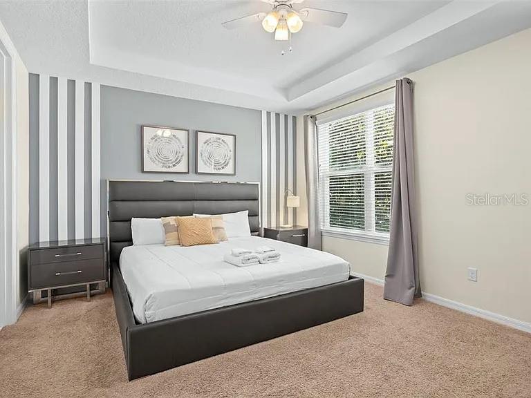 A bedroom features a gray upholstered bed, striped accent wall, and a ceiling fan — 1521 CAREY PALM CIRCLE, KISSIMMEE, FL