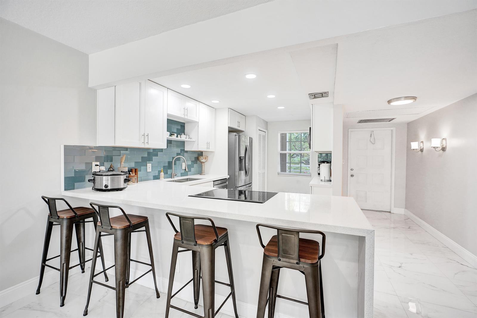 A kitchen features white cabinets, a blue tile backsplash, and a breakfast bar with stools — 545 Oaks Lane # 204, Pompano Beach FL 33069, POMPANO BEACH, FL