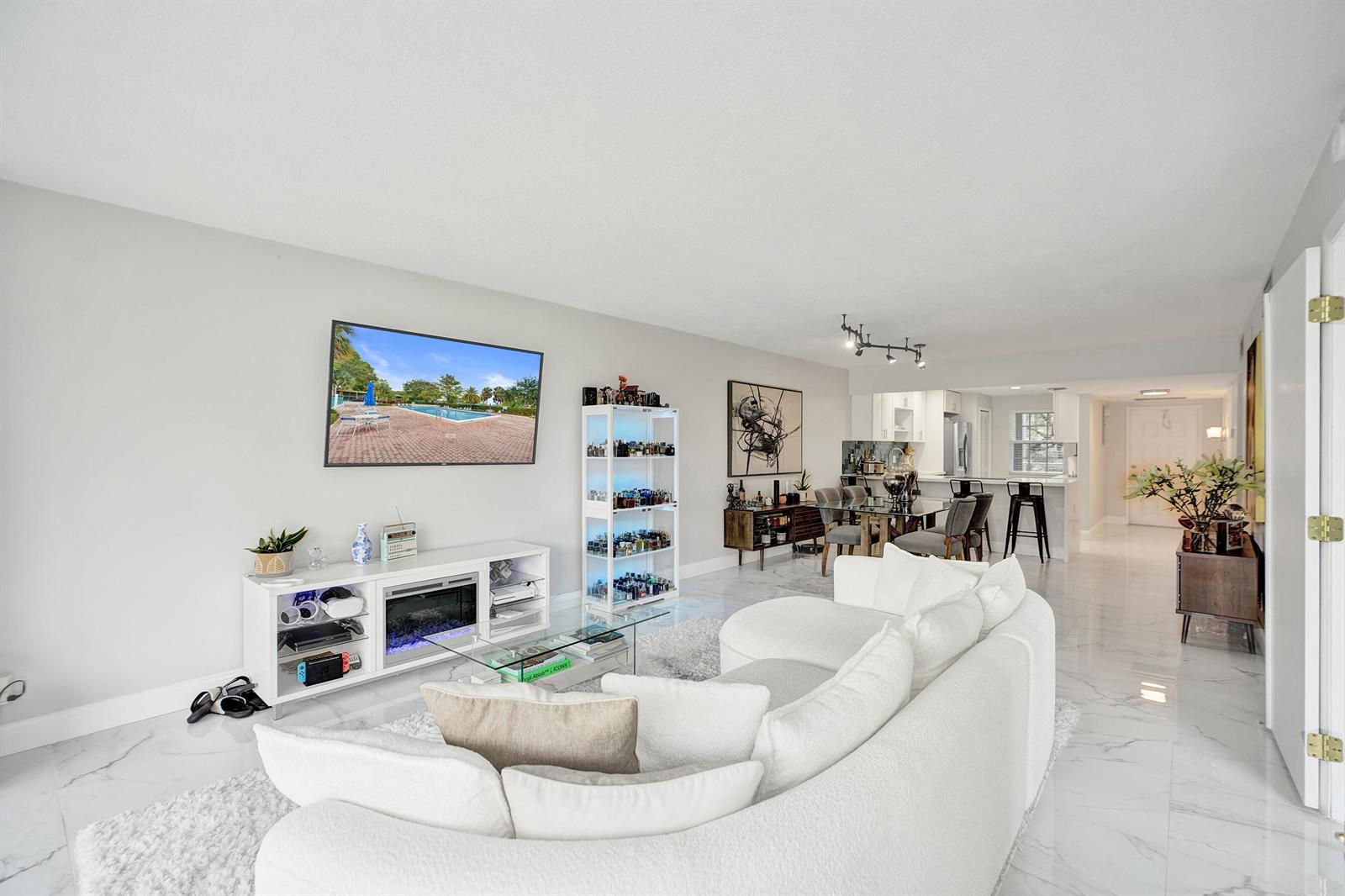 A bright living room features white marble floors, a curved sofa, and a wall-mounted television — 545 Oaks Lane # 204, Pompano Beach FL 33069, POMPANO BEACH, FL