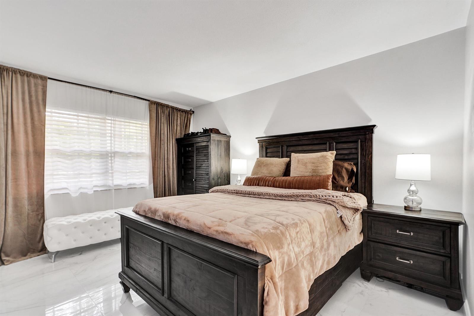 A bedroom features a dark wood bed frame, matching nightstand, and a white tufted bench — 545 Oaks Lane # 204, Pompano Beach FL 33069, POMPANO BEACH, FL