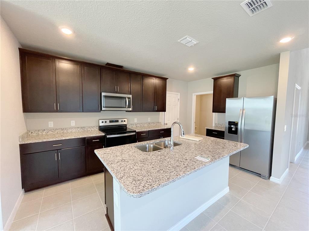 A kitchen with dark wood cabinets, granite countertops, a center island, and stainless steel appliances — 3157 BELLA VISTA DRIVE, DAVENPORT, FL