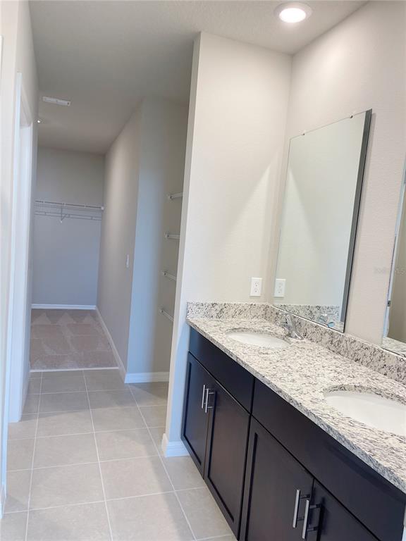 A bathroom features a double vanity with dark cabinets, granite countertops, and an adjacent walk-in closet — 3157 BELLA VISTA DRIVE, DAVENPORT, FL