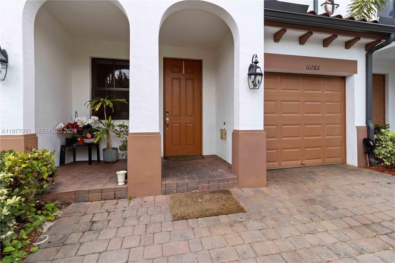 The exterior of a home features a brick driveway, a brown garage door, and an arched entryway — 10268 NW 88th Ter, Doral FL 33178, DORAL, FL