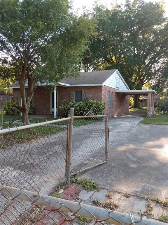 A single-story brick house with a front porch and an attached carport behind a chain-link fence — 110 ORANGE AVENUE, WINTER HAVEN, FL