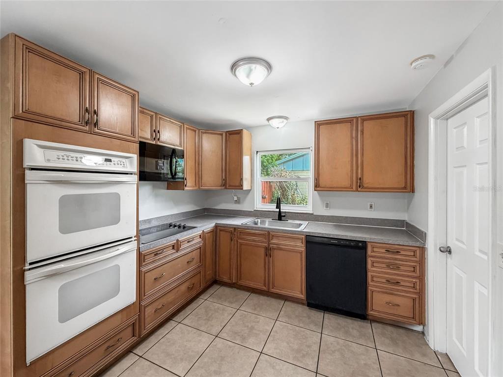 A kitchen features wood cabinets, white double ovens, a black dishwasher, and tile flooring — 602 18TH STREET, ORLANDO, FL