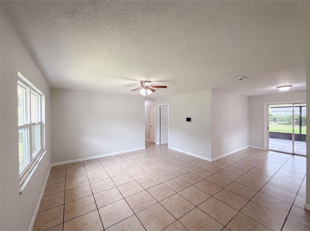 An empty living area with beige tile flooring, a ceiling fan, and sliding glass doors — 602 18TH STREET, ORLANDO, FL