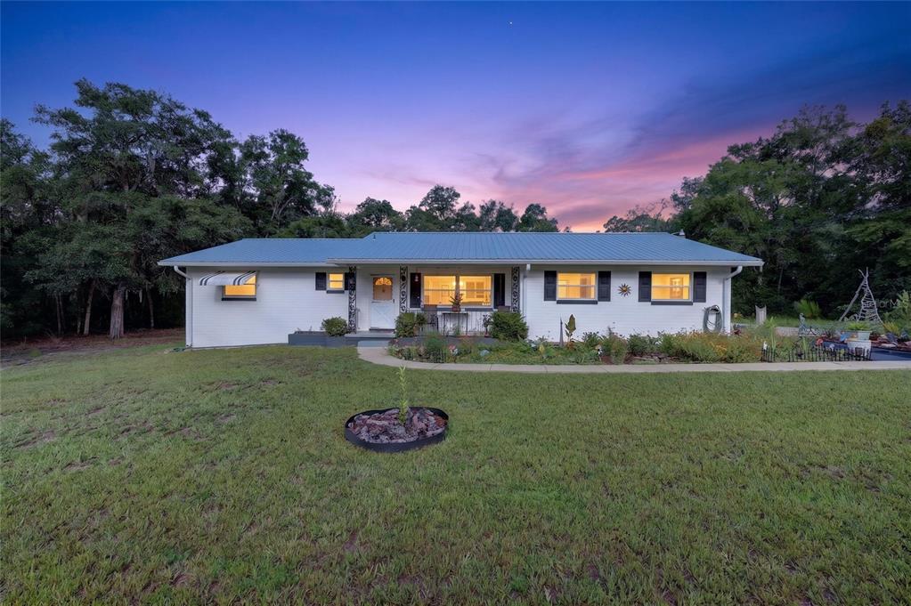 A single-story white house with a metal roof sits on a grassy lot at dusk — 4500 SW FRESHWATER COURT, DUNNELLON, FL