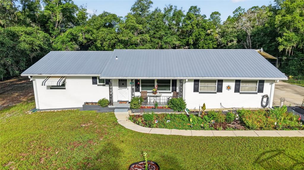 A white, single-story house with a gray metal roof sits behind a landscaped front yard — 4500 SW FRESHWATER COURT, DUNNELLON, FL