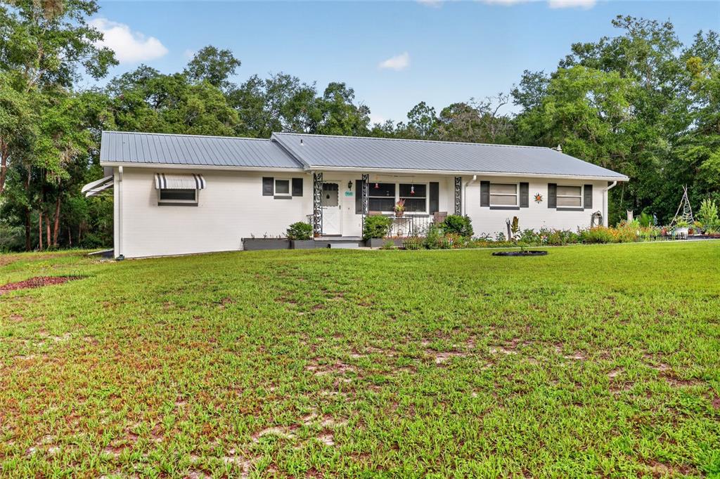 A single-story white house with a metal roof sits on a grassy lawn — 4500 SW FRESHWATER COURT, DUNNELLON, FL