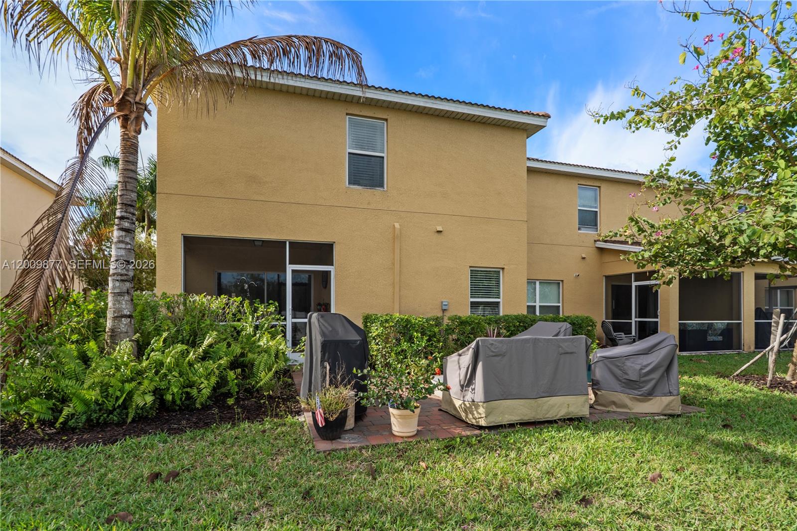 The exterior of a two-story yellow house features a brick patio and screened-in porches — FORT MYERS, FL