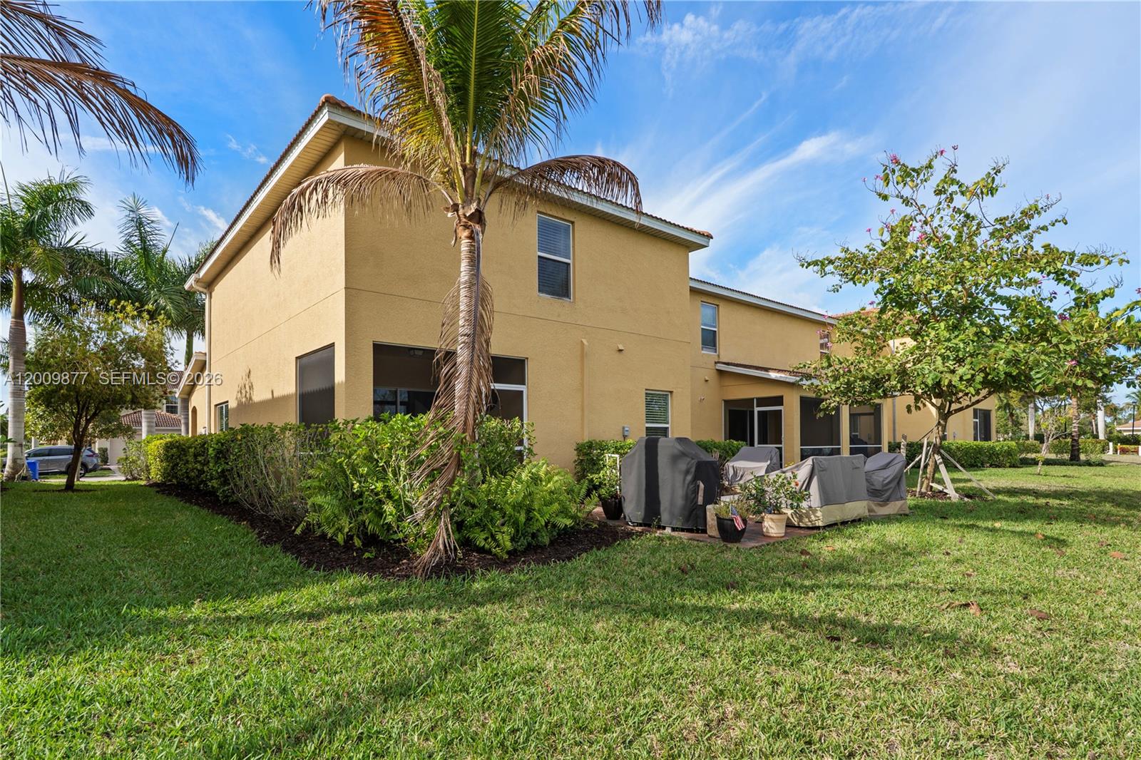 The exterior of a two-story yellow house features a grassy yard and a patio area — FORT MYERS, FL