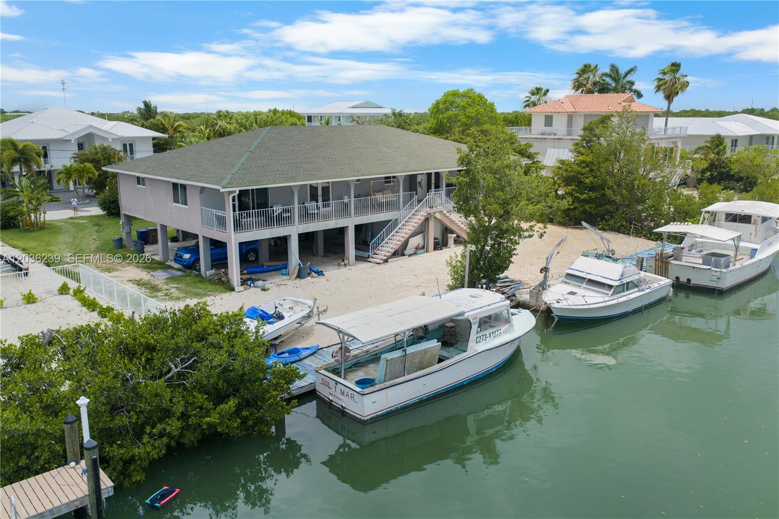An elevated house with a porch and stairs sits beside a canal with several docked boats — 2100 Avenue H, Marathon FL 33050, MARATHON, FL