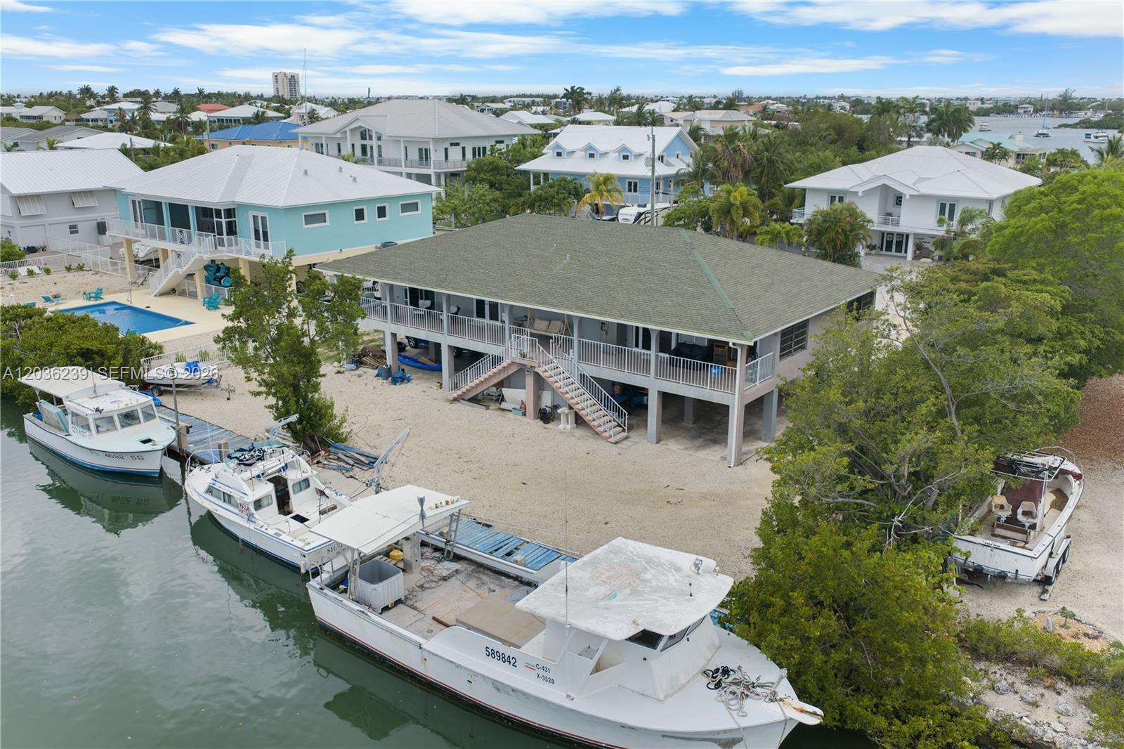 An elevated house with a green roof sits on a sandy lot beside a canal — 2100 Avenue H, Marathon FL 33050, MARATHON, FL