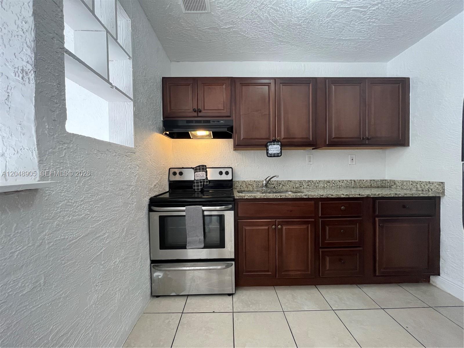 A kitchen features dark wood cabinets, stainless steel appliances, granite countertops, and white textured walls — 3028 NW 2nd St, Pompano Beach FL 33069, POMPANO BEACH, FL