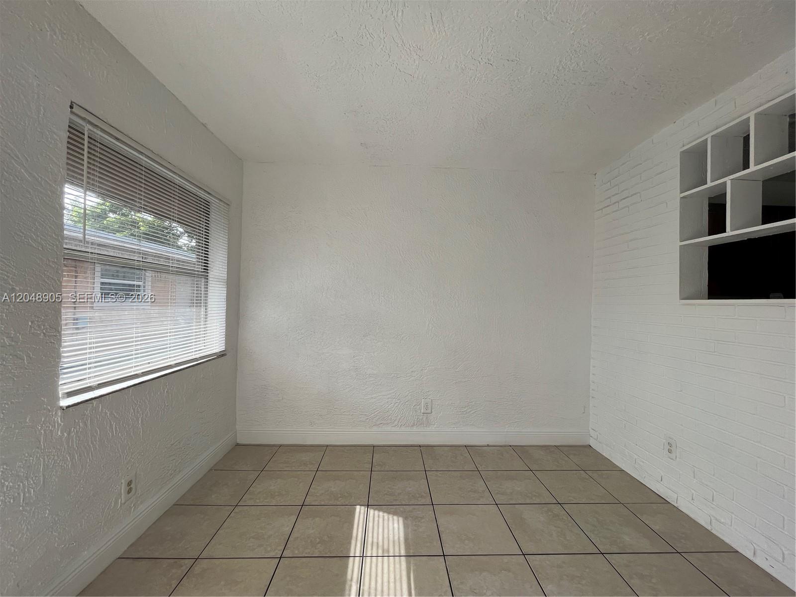A small room features white textured walls, beige tile flooring, and a window with blinds — 3028 NW 2nd St, Pompano Beach FL 33069, POMPANO BEACH, FL