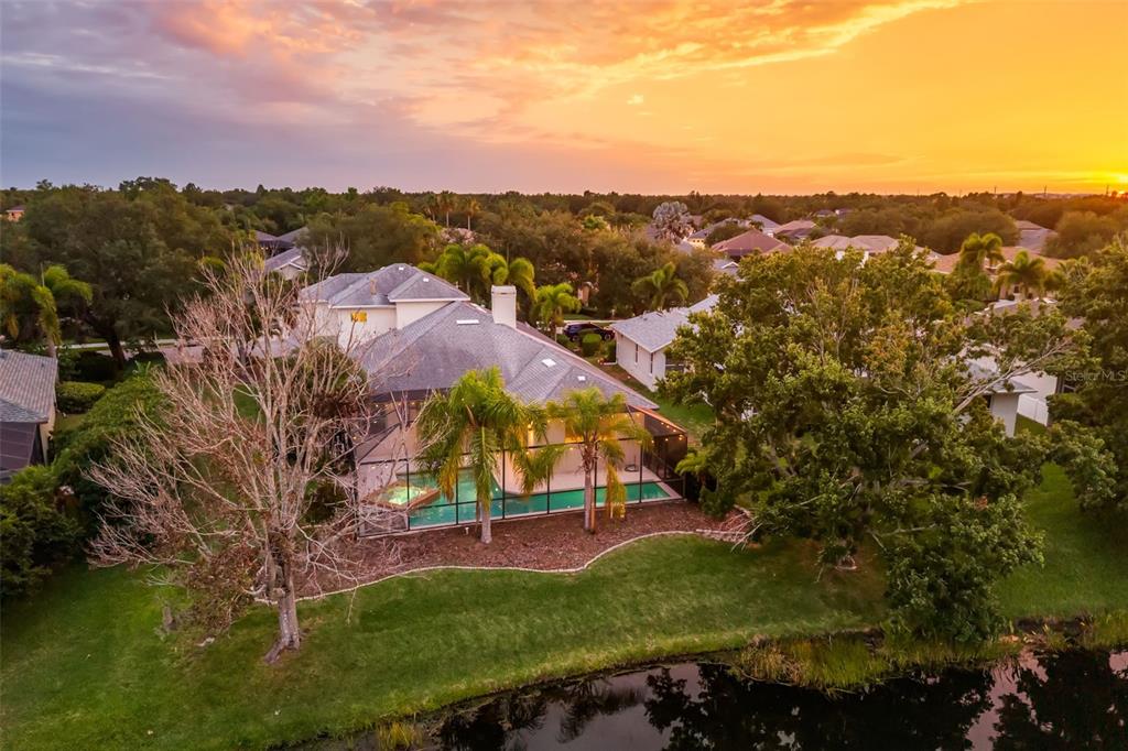 An aerial view of a house with a screened-in pool overlooking a pond at sunset — 6215 WARBLER LANE, LAKEWOOD RANCH, FL