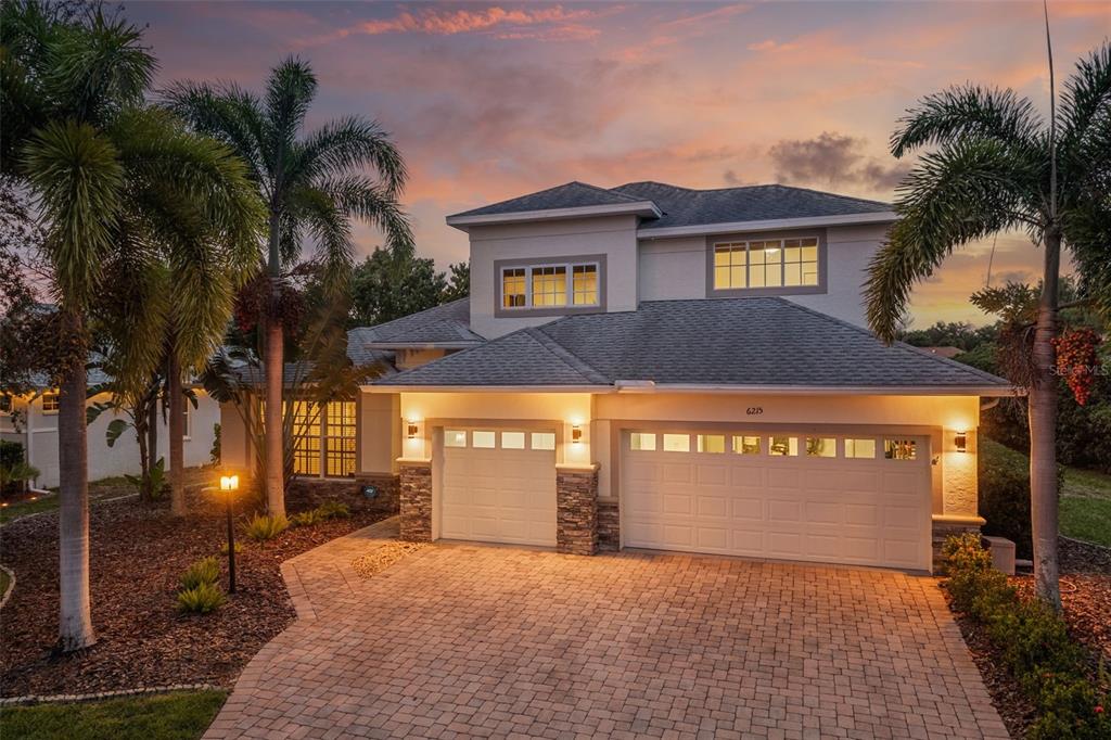 A two-story house with a paved driveway, stone accents, and palm trees at dusk — 6215 WARBLER LANE, LAKEWOOD RANCH, FL