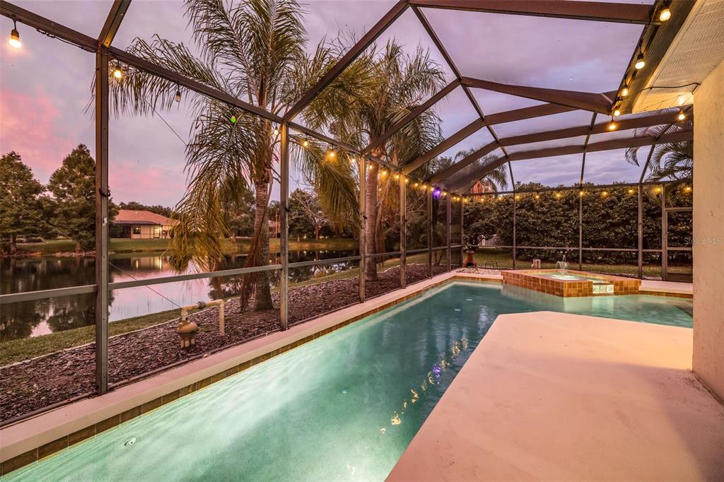 A screened-in pool and hot tub overlook a lake at sunset — 6215 WARBLER LANE, LAKEWOOD RANCH, FL