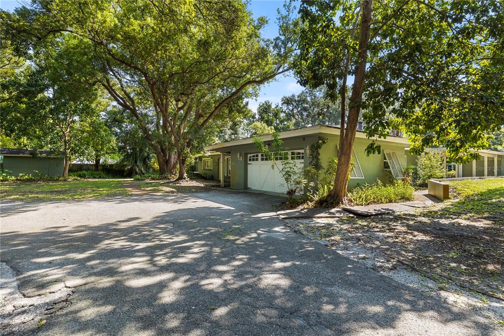 A green single-story house with a white garage door sits on a large, tree-shaded lot — 2162 LONG BOW LANE, CLEARWATER, FL