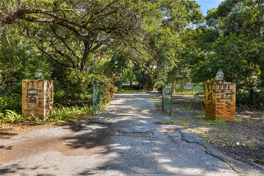 A paved driveway leads through a gated entrance flanked by two brick pillars with lanterns — 2162 LONG BOW LANE, CLEARWATER, FL