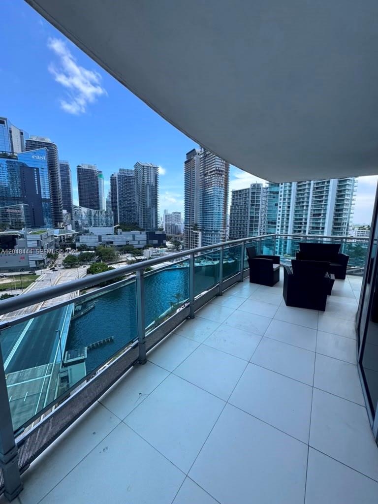 A balcony with white tile flooring overlooks a canal and a city skyline — 350 S Miami Ave # 1902, Miami FL 33130, MIAMI, FL