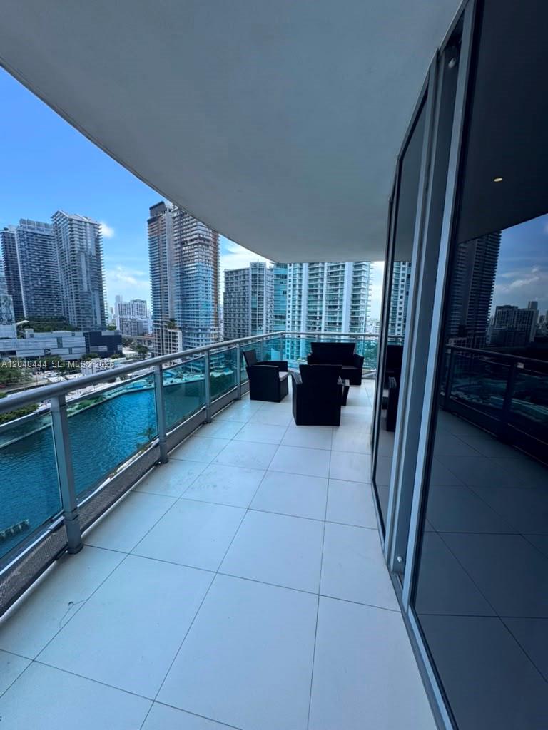 A high-rise balcony features white tile flooring, black patio furniture, and a glass railing — 350 S Miami Ave # 1902, Miami FL 33130, MIAMI, FL