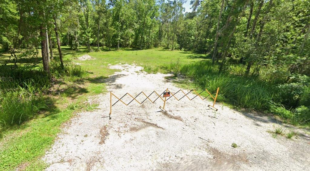 A gravel driveway leads to a grassy, wooded lot blocked by a portable folding barrier — 0 RAY BROWNING ROAD, BROOKSVILLE, FL