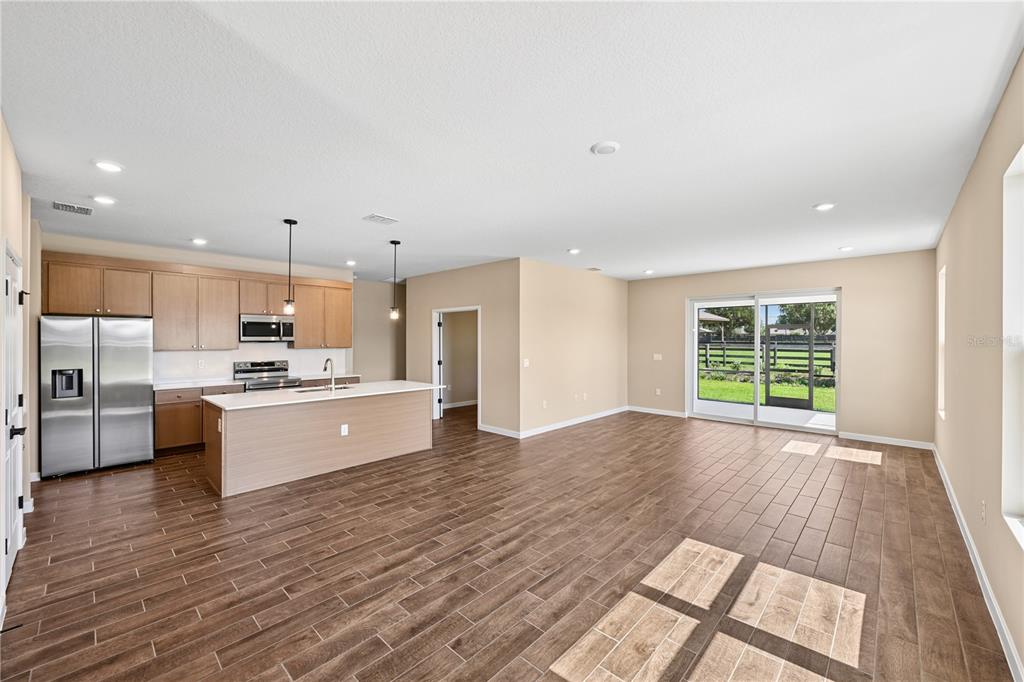 An open-concept kitchen and living area with wood-look tile flooring and sliding glass doors — 4497 NW 37TH STREET, OCALA, FL