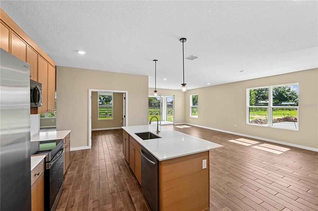 A kitchen with wood cabinets and a center island overlooks an open-concept living area — 4497 NW 37TH STREET, OCALA, FL