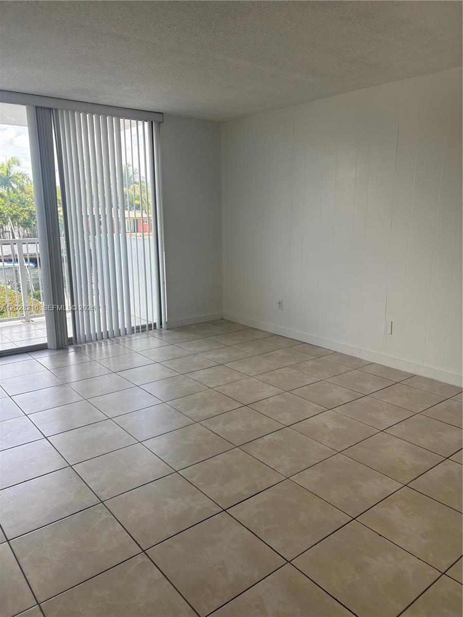 An empty room with beige tile flooring, white walls, and vertical blinds covering a balcony door — 2000 NE 135th St # 208, North Miami FL 33181, NORTH MIAMI, FL