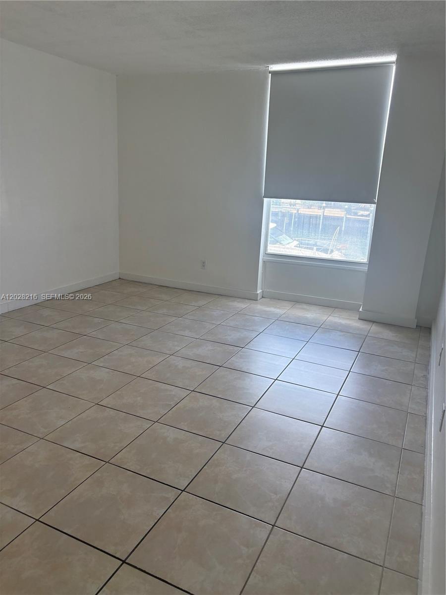 An empty room features light-colored tile flooring, white walls, and a window with a roller shade — 2000 NE 135th St # 208, North Miami FL 33181, NORTH MIAMI, FL