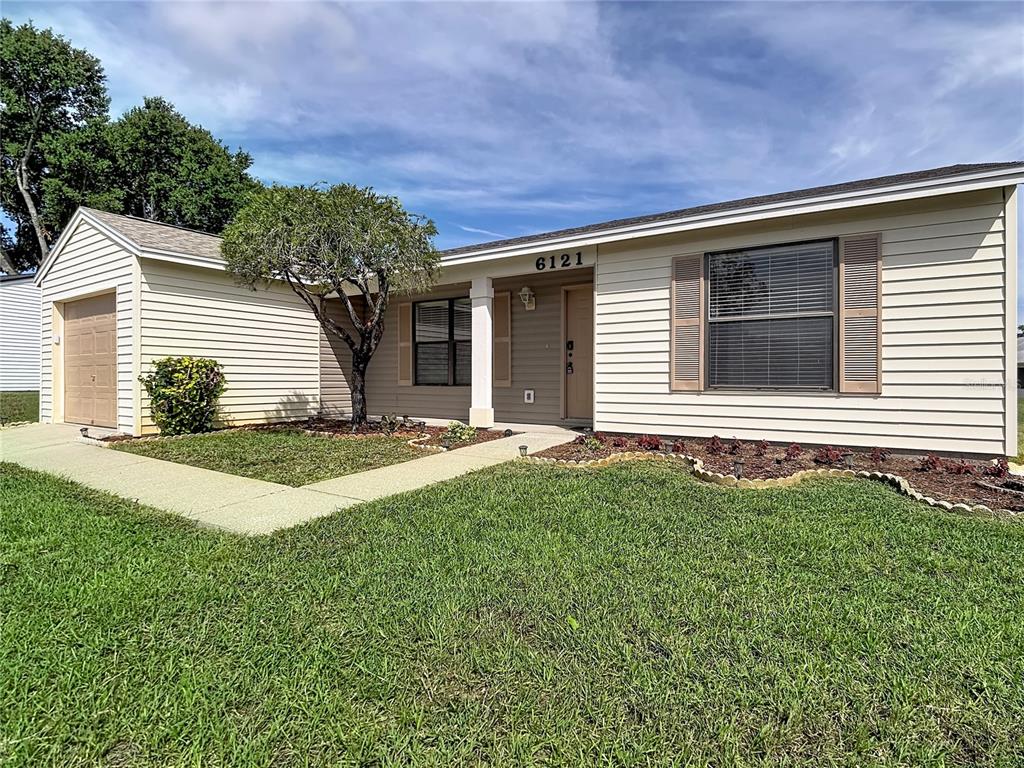 A single-story house with light-colored horizontal siding, a garage, and a small front yard — 6121 KITTIWAKE DRIVE, LAKELAND, FL