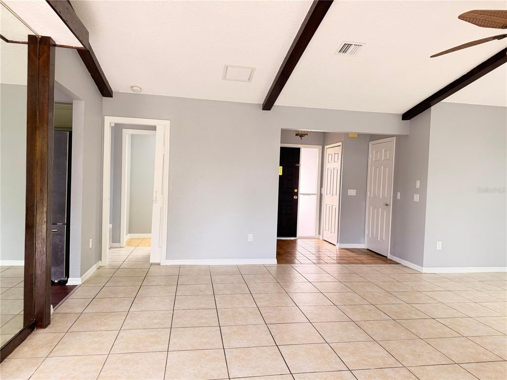 A living room features light tile flooring, gray walls, exposed ceiling beams, and multiple doorways — 21105 HIGGS DRIVE, PORT CHARLOTTE, FL