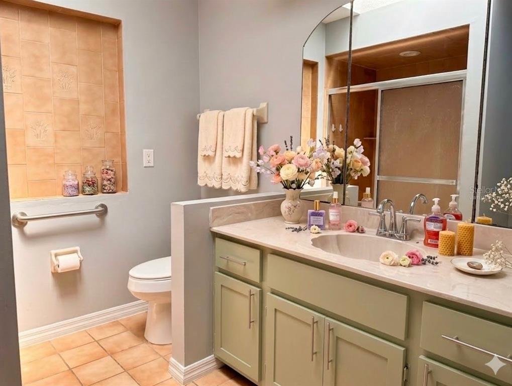 A bathroom features a sage green vanity, a toilet area with a grab bar, and tile — 21105 HIGGS DRIVE, PORT CHARLOTTE, FL