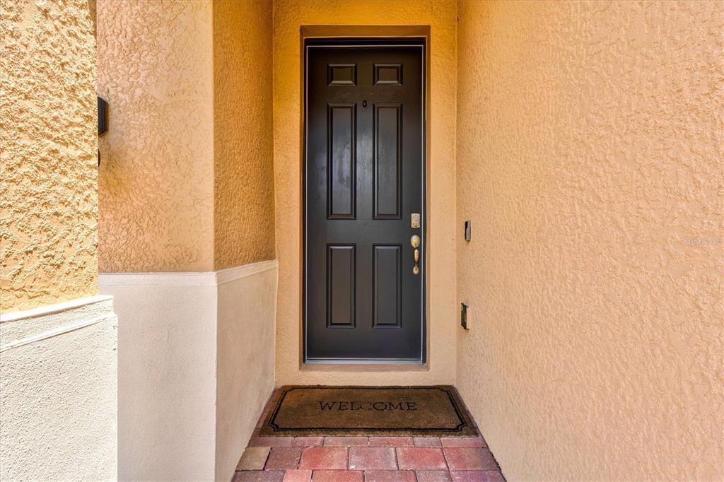 A dark front door with a welcome mat sits in a recessed entryway with stucco walls — 308 SOLIERA STREET, NOKOMIS, FL