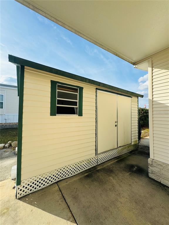 A beige storage shed with green trim and double doors sits on a concrete patio — 917 ST GEORGE DRIVE, DAVENPORT, FL