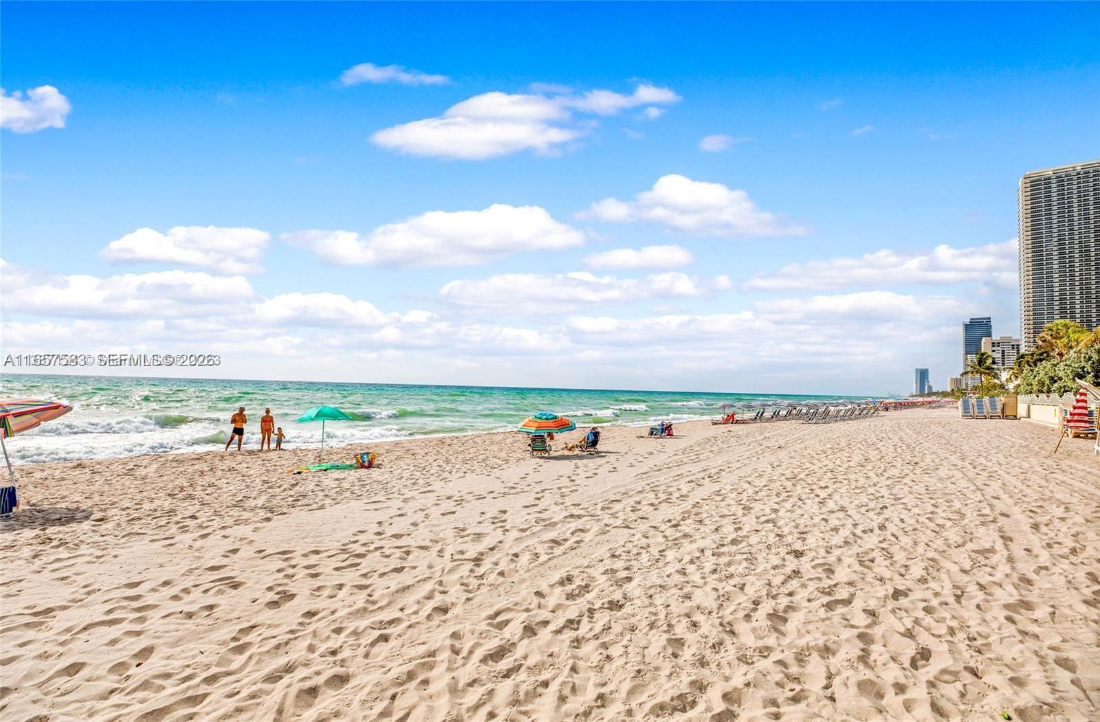 A sandy beach stretches along the ocean with several umbrellas and high-rise buildings nearby — 3801 S Ocean Dr # 12M, Hollywood FL 33019, HOLLYWOOD, FL