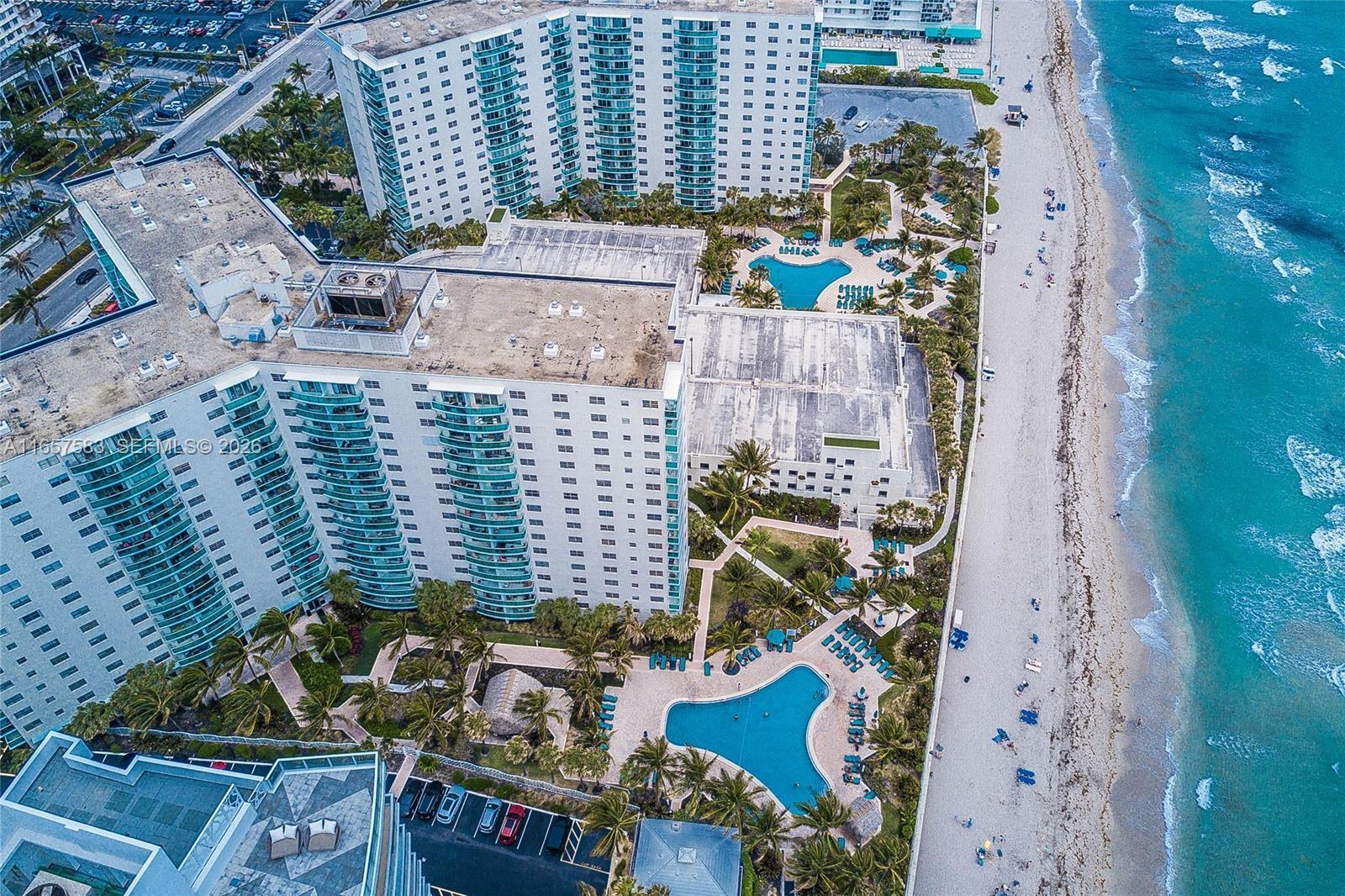 An aerial view shows two large residential buildings with swimming pools located beside a sandy beach — 3801 S Ocean Dr # 12M, Hollywood FL 33019, HOLLYWOOD, FL