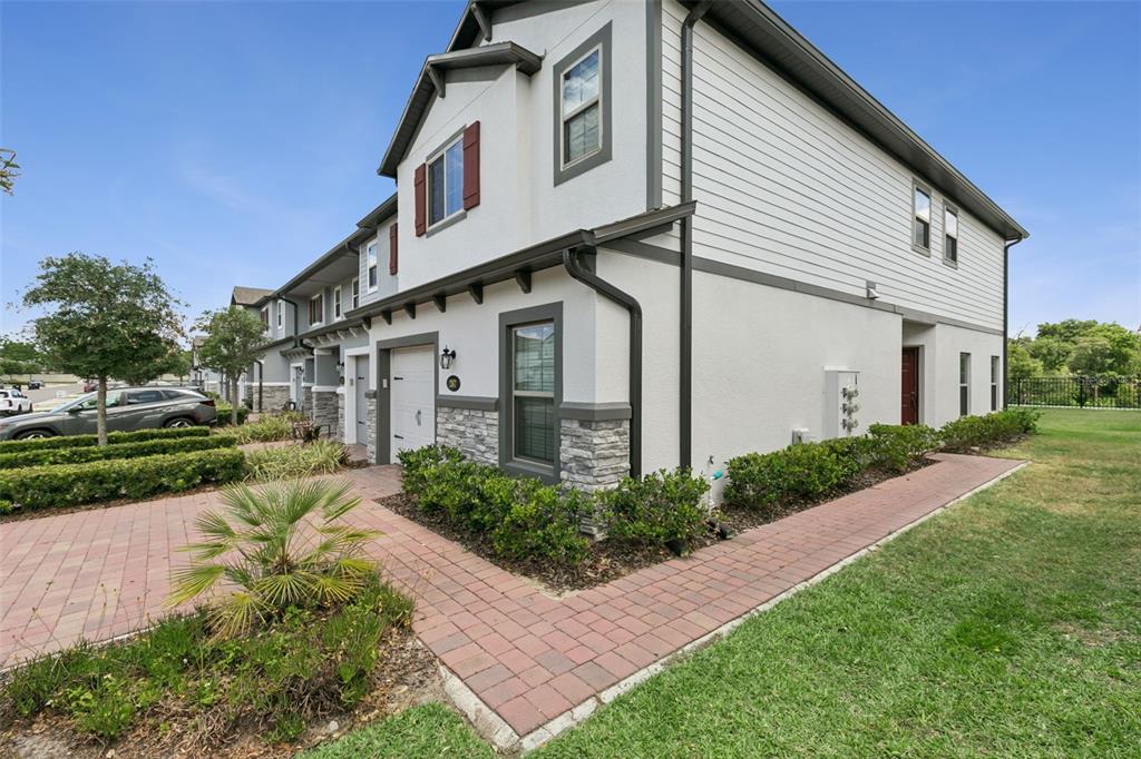 A multi-story townhouse exterior features white siding, stone accents, and a brick paver walkway — 267 SMUGGLERS WAY, APOPKA, FL