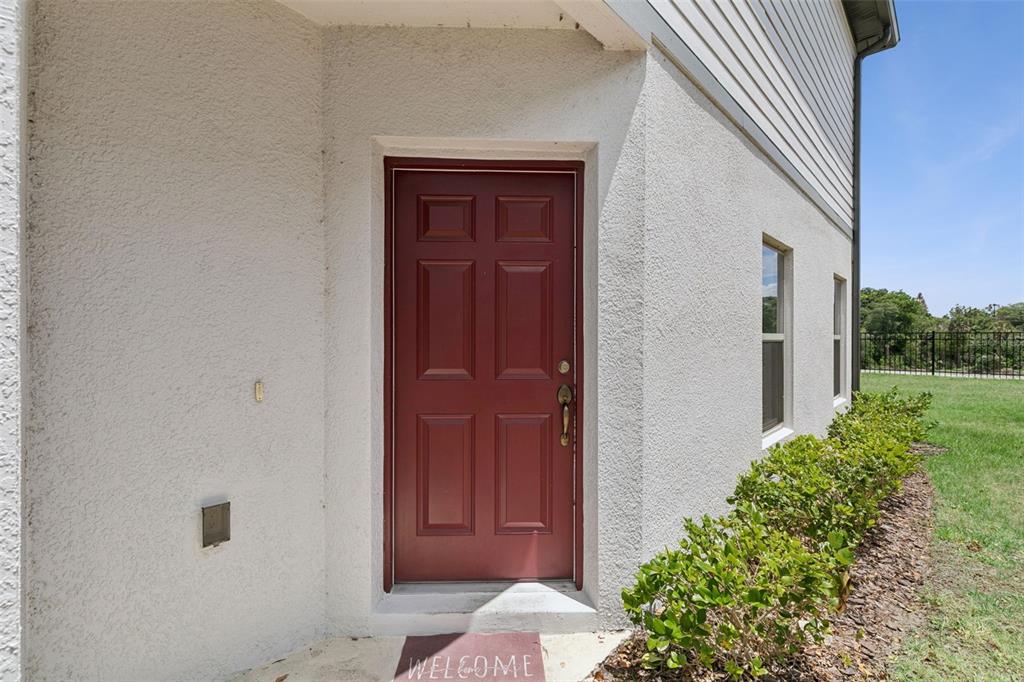 A red front door is set into a white stucco exterior wall with a welcome mat — 267 SMUGGLERS WAY, APOPKA, FL
