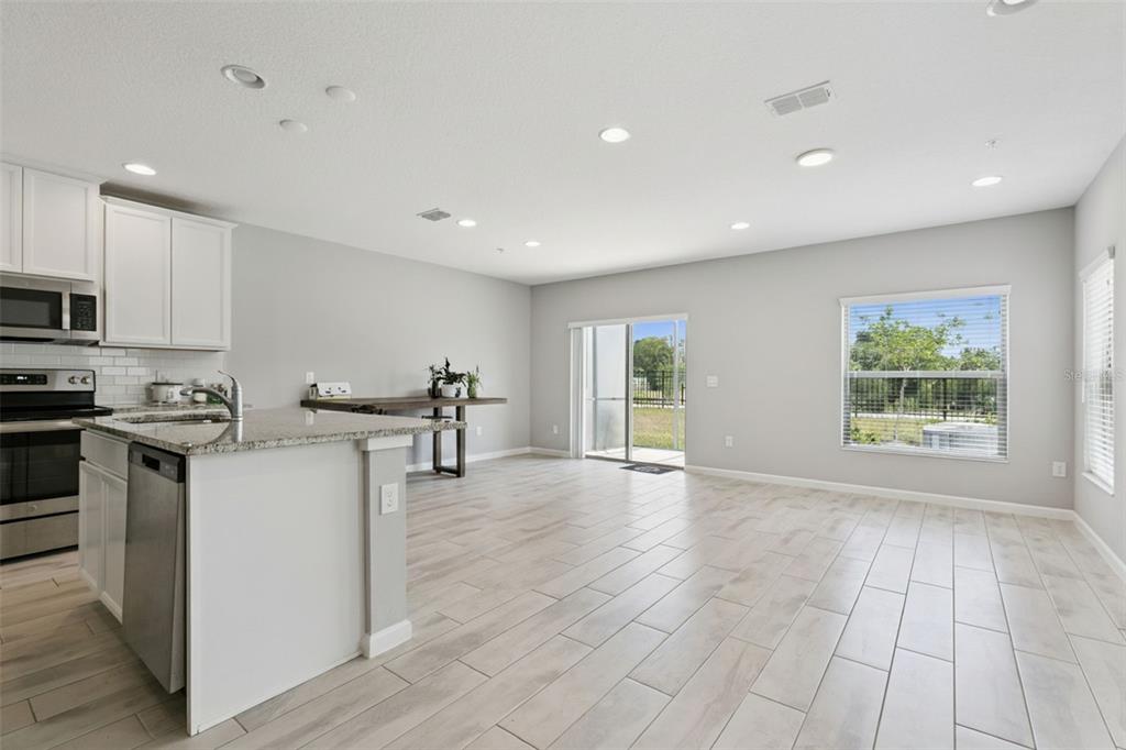An open-concept kitchen and living area featuring light wood-look tile floors and white cabinetry — 267 SMUGGLERS WAY, APOPKA, FL