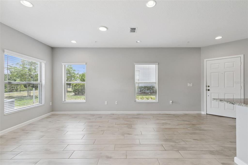 An empty room with light wood-look tile flooring, gray walls, recessed lighting, and three windows — 267 SMUGGLERS WAY, APOPKA, FL