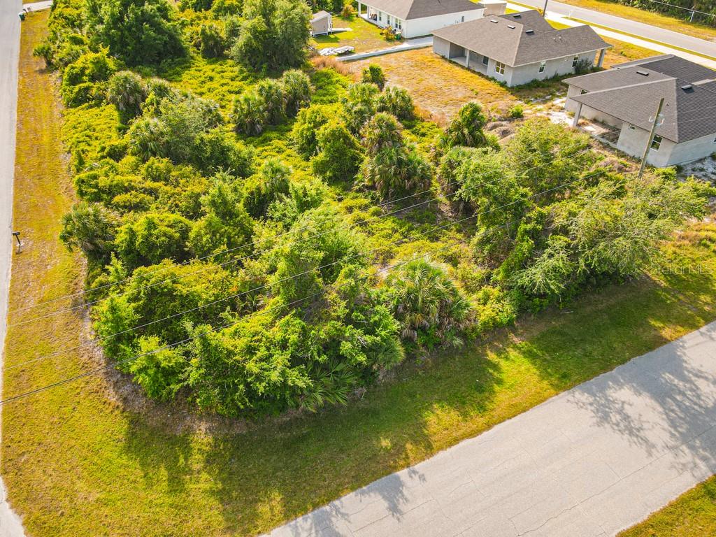 An aerial view shows a vacant, heavily wooded residential lot bordered by two paved roads — 13369 GALVESTON AVENUE, PORT CHARLOTTE, FL