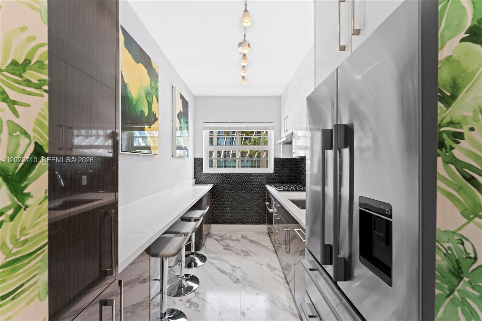 A narrow galley kitchen features white countertops, dark cabinetry, a marble floor, and bar seating — 1925 Washington Ave # 16, Miami Beach FL 33139, MIAMI BEACH, FL