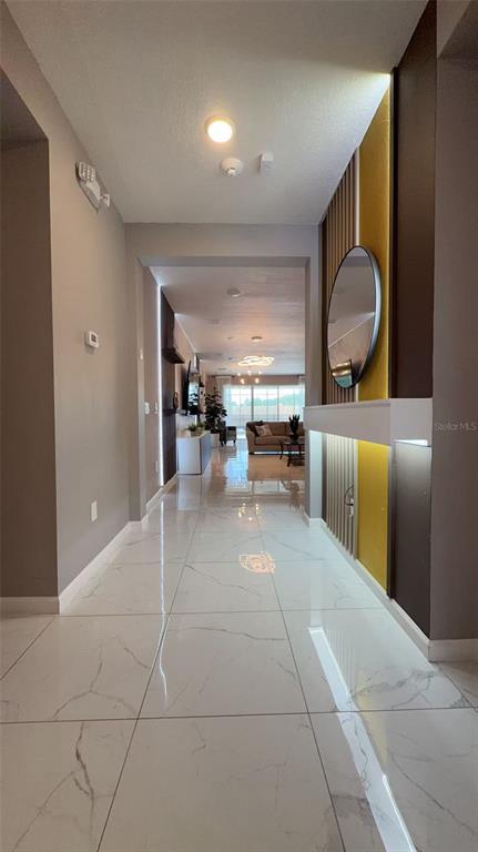 A hallway with white marble-look tile flooring leads toward a living room with modern decor — 3820 SONOMA BOULEVARD, KISSIMMEE, FL